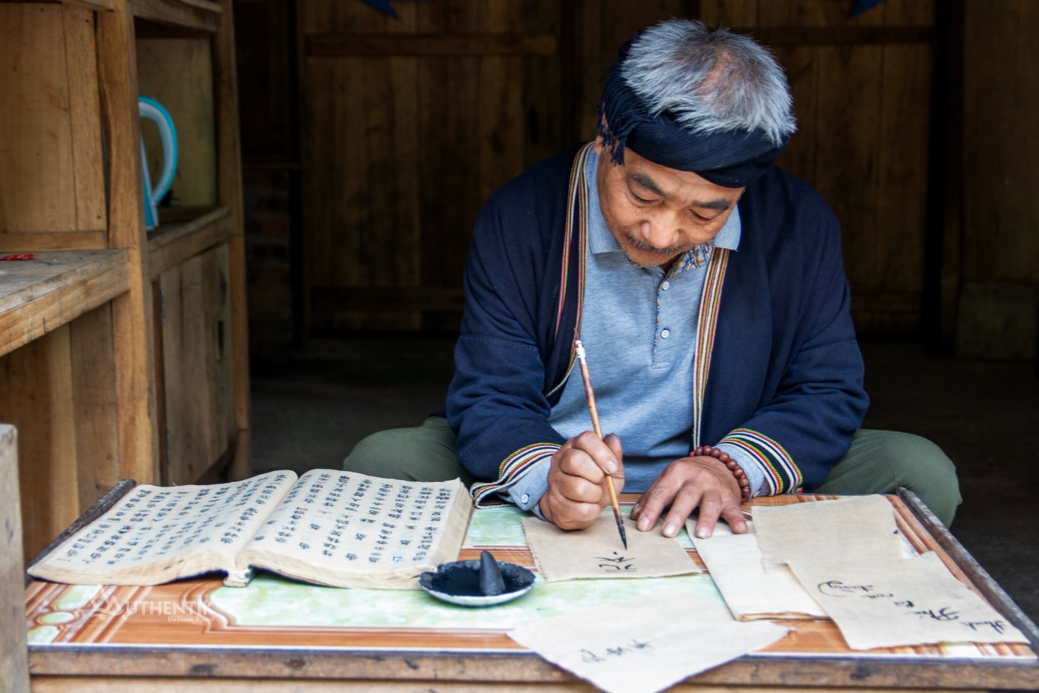 Dao Tien artisan writing Dao Nom script on handmade D&oacute; paper in Xom Sung Village