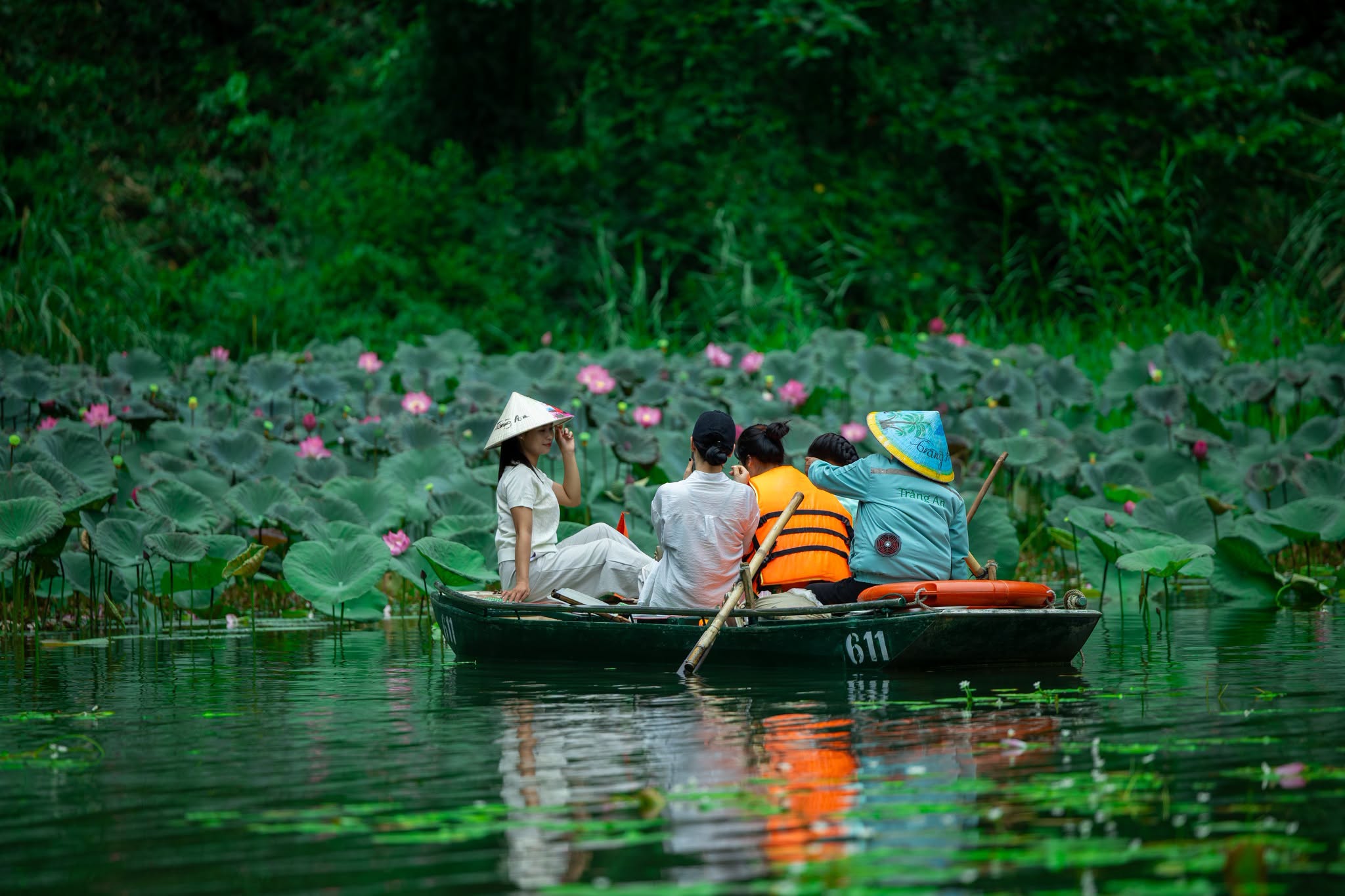 Traditional boat passing lotus ponds in Trang An surrounded by towering limestone mountains (Cre: Di Sản Tr&agrave;ng An)